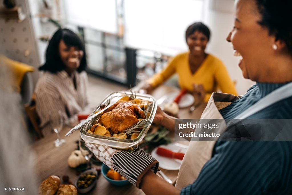 Woman serving roasted turkey to friends at home