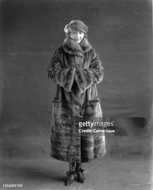 Female model standing in front of a backdrop wearing a full fur coat and a small hat. Circa 1935