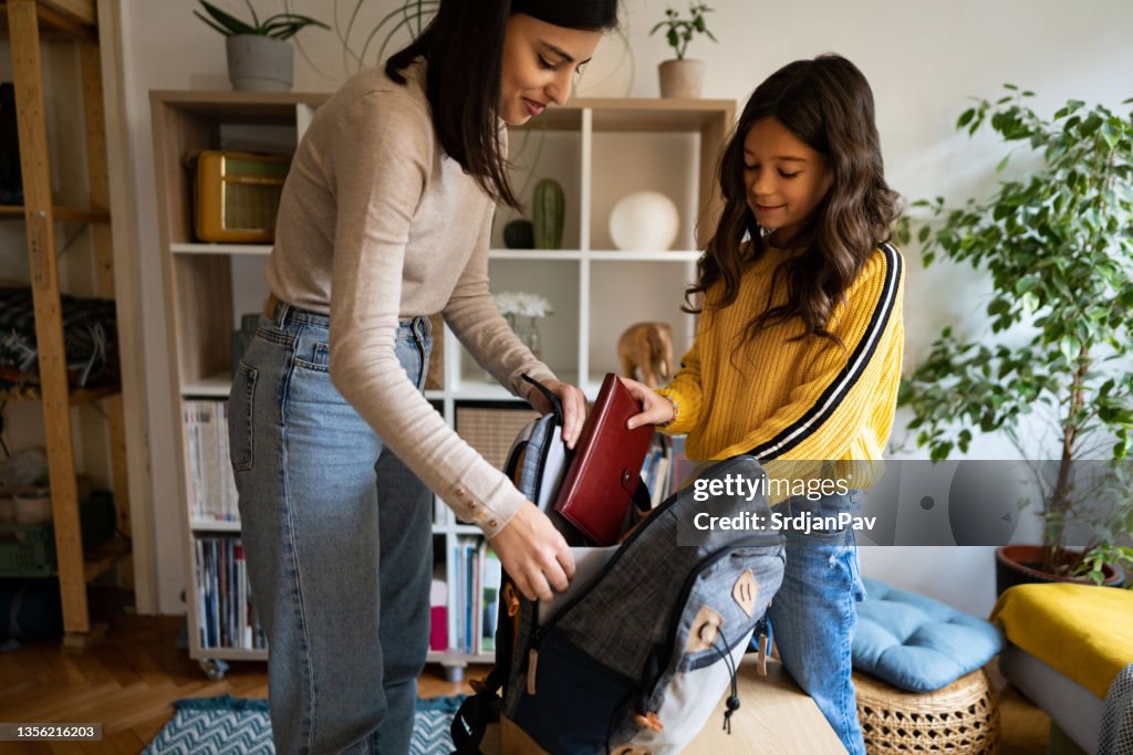 Schoolgirl, packing her backpack with school supplies with a help of her mother