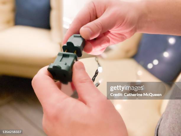 man plugging strings of electric christmas lights together - enchufar fotografías e imágenes de stock