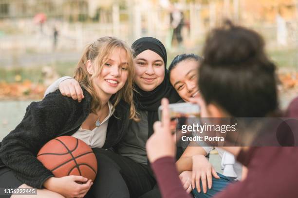 mädchen fotografiert freunde mit telefon auf basketballplatz - ethnische integration deutschland stock-fotos und bilder