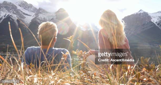 casal de caminhadas relaxa em cume de montanha gramado - canmore - fotografias e filmes do acervo