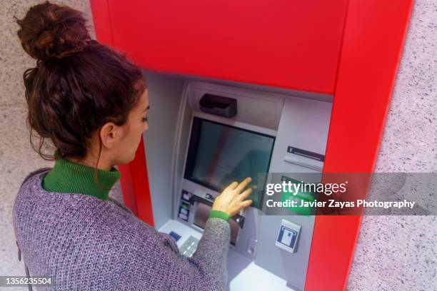 curly hair woman using an atm in the city - paid absence stock pictures, royalty-free photos & images