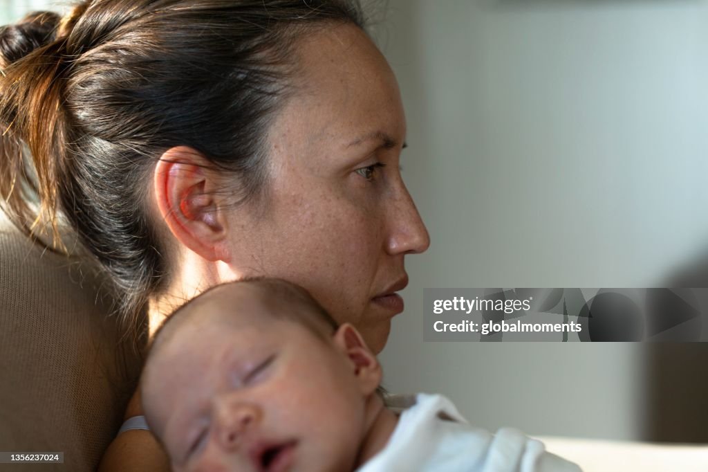 A sad mother sitting at home suffering from postpartum depression. Motherhood problems.