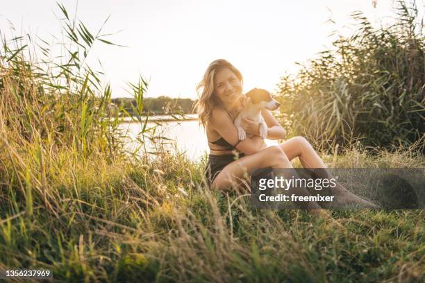 smiling woman sitting in tall grass in nature and embracing her dog - long grass bildbanksfoton och bilder