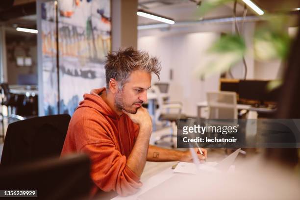junger mann, der im büro am computer arbeitet - designer einrichtung stock-fotos und bilder