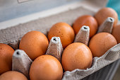 Closeup macro of pasture raised farm fresh dozen brown eggs store bought from farmer in carton box container with speckled eggshells texture