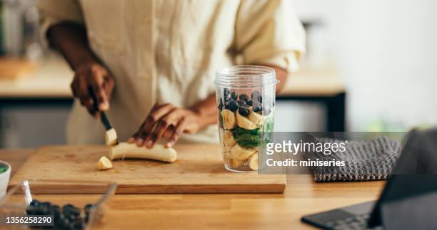 close up of woman hands cutting banana on a cutting board - smoothies stockfoto's en -beelden