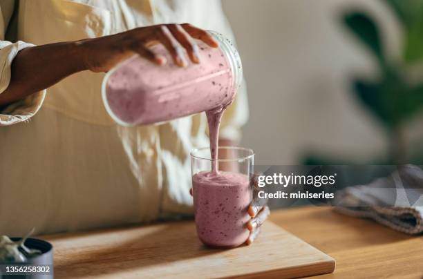 anonymous afro-american woman pouring a smoothie into a glass - smoothie and woman stockfoto's en -beelden