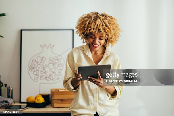 afroamerikanische frau, die steht und lächelt, während sie auf ein digitales tablet schaut - e reader stock-fotos und bilder
