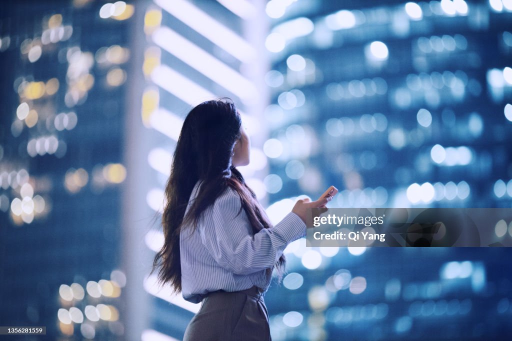 Young Asian woman standing in Shanghai financial district using her smartphone