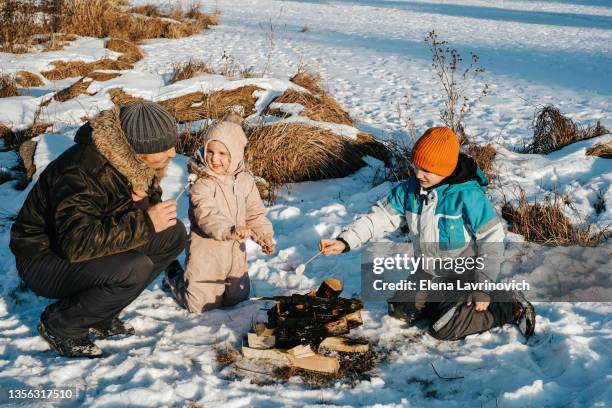 father with his daughter on a picnic in winter. tourism with children. a family fry marshmallows on a campfire in the winter on the snow. - bbq winter ストックフォトと画像