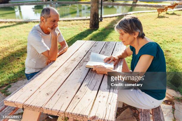 senior adult sitting in park bench and reading analog book - wooden bench stock pictures, royalty-free photos & images