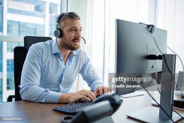software developer working on the computer, wearing headset - headset imagens e fotografias de stock