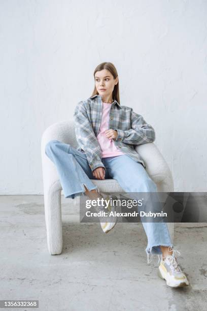 stylish young brunette woman posing sitting in a chair in casual clothes - chairs in studio stock pictures, royalty-free photos & images