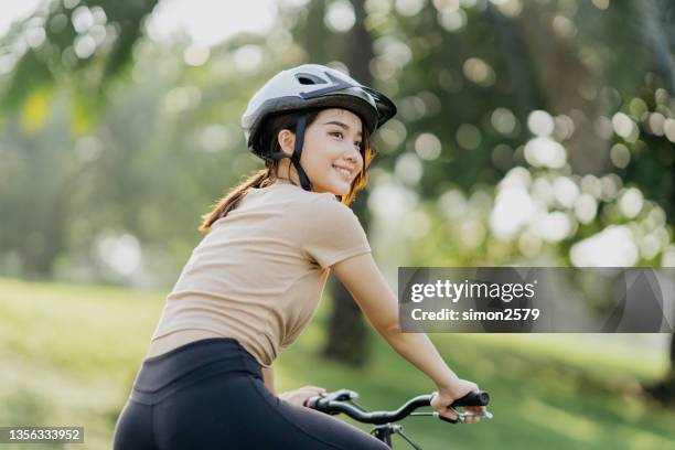 young healthy woman exercising on bicycle in public park - bicycle safety light stockfoto's en -beelden