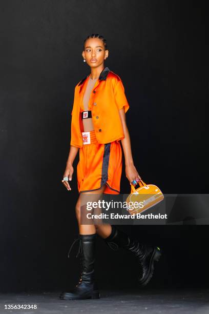 Model wears an orange shiny satin V-neck cropped top, an orange shiny satin high waist puffy shorts, an orange shiny puffy short sleeves,...