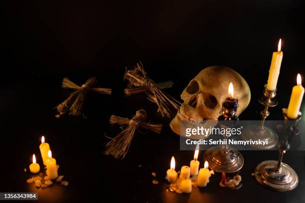 old skull and candle with incense on old altar plate which has dim light. select focus, black background. straw voodoo dolls. copy space - bruja fotografías e imágenes de stock