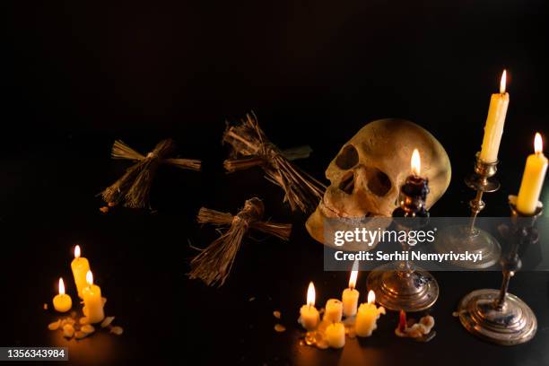 old skull and candle with incense on old altar plate which has dim light. select focus, black background. straw voodoo dolls. copy space - witch imagens e fotografias de stock