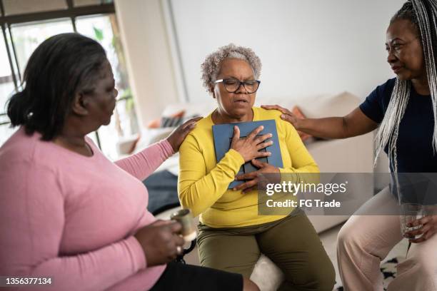 sad senior woman with a photo frame and being consoled by friends at home - 寡婦 個照片及圖片檔