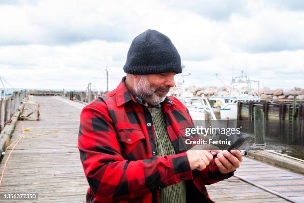 a fisherman on a wharf using his mobile phone. - fisherman bildbanksfoton och bilder