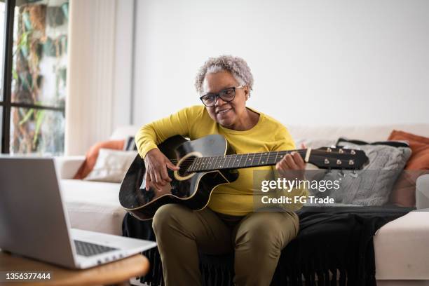 senior woman learning to play guitar at an online class at home - learn guitar stockfoto's en -beelden