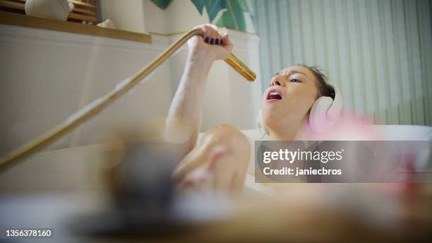 young woman taking a bubble bath in her bathroom. singing to a hand shower - singing shower stock pictures, royalty-free photos & images