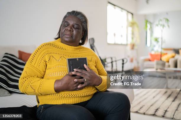 senior woman holding a picture frame missing someone at home - widow stock pictures, royalty-free photos & images