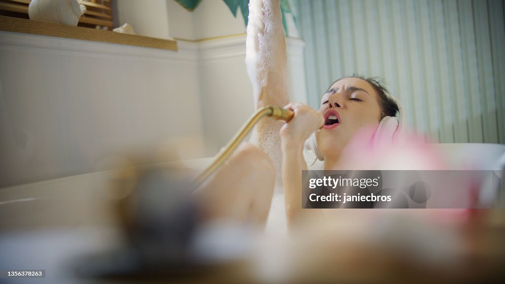 Junge Frau nimmt ein Schaumbad in ihrem Badezimmer. Singen zur Handbrause