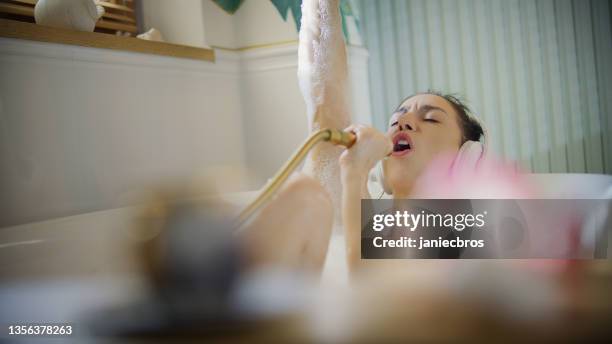 young woman taking a bubble bath in her bathroom. singing to a hand shower - woman shower bath imagens e fotografias de stock