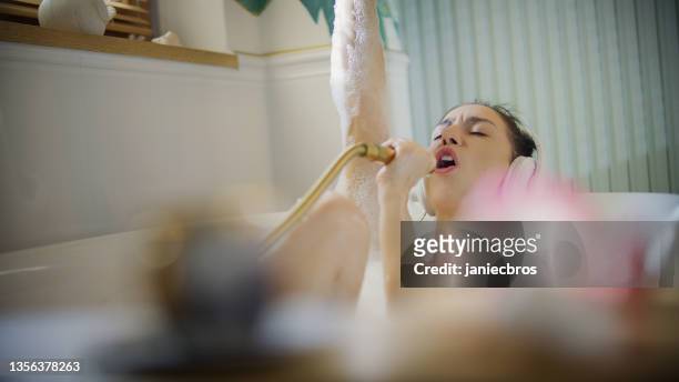 young woman taking a bubble bath in her bathroom. singing to a hand shower - dusch bildbanksfoton och bilder