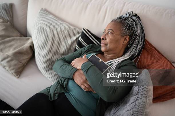 senior woman holding a picture frame missing someone at home - widow pension stock pictures, royalty-free photos & images