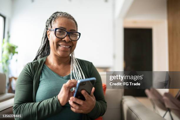 porträt einer älteren frau, die zu hause ein mobiltelefon benutzt - african american ethnicity stock-fotos und bilder