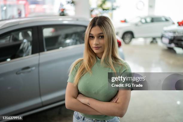 portrait of a young woman in front of a car in a car dealership - buying a car 個照片及圖片檔