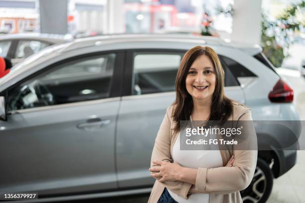portrait of a happy mature woman in front of a car in a car dealership - 僅成年女人 個照片及圖片檔