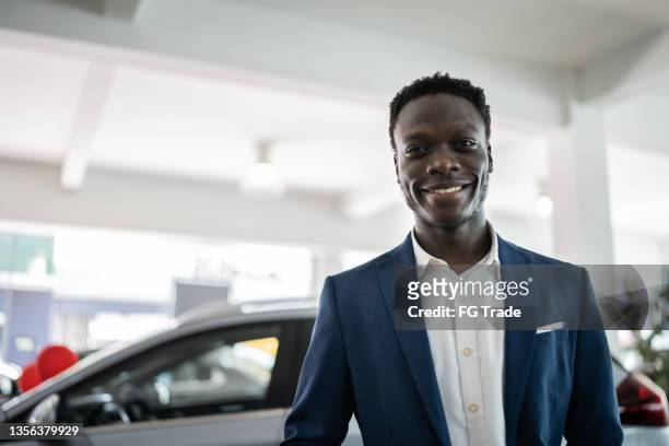portrait of a confident car dealer in a showroom - car salesman stock pictures, royalty-free photos & images