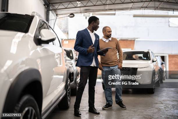 salesman showing car to customer in a car dealership - rental assistance stock pictures, royalty-free photos & images