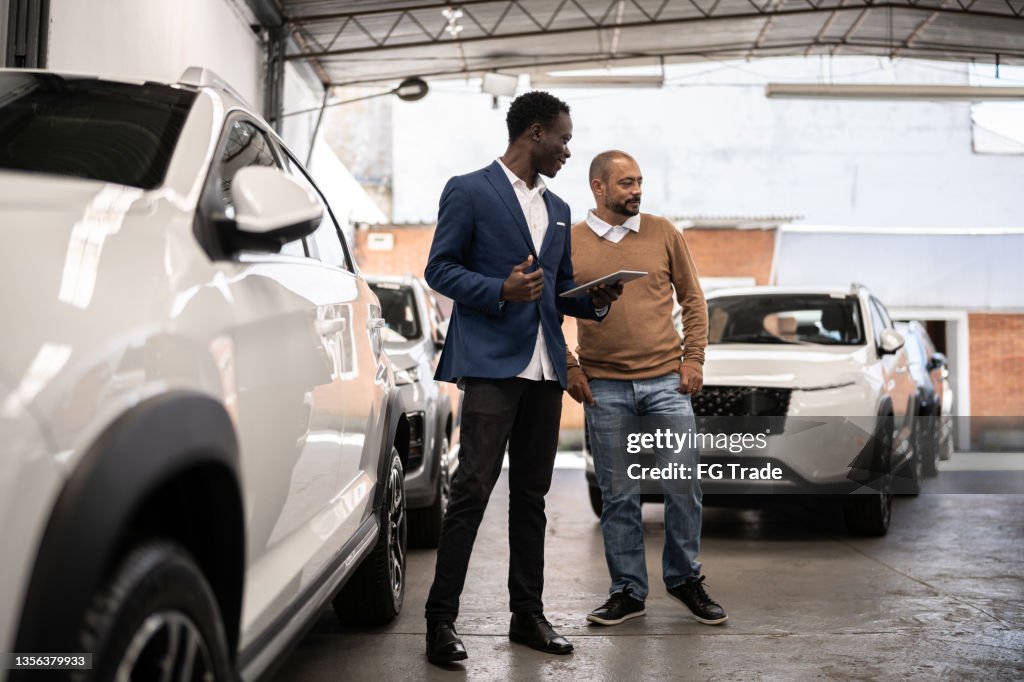 Vendedor mostrando carro para cliente em uma concessionária de carros