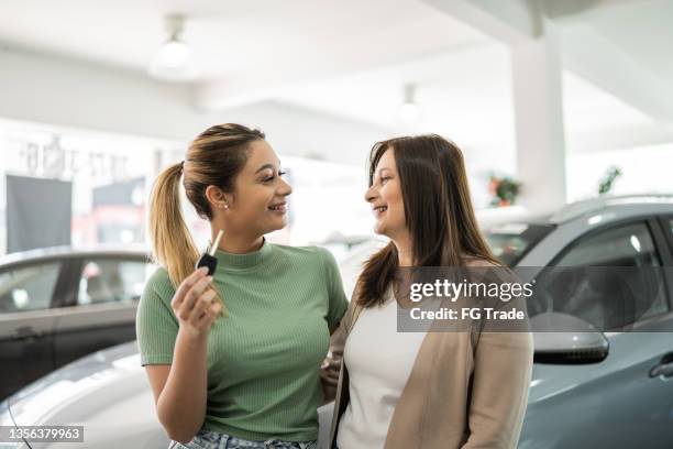 glückliches teenger-mädchen mit ihrer mutter, die in einem autohaus die schlüssel eines neuen autos zeigt - new mum stock-fotos und bilder