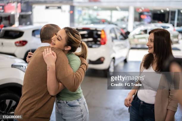 father embracing teenager daughter in a car dealership - buying a car stock pictures, royalty-free photos & images