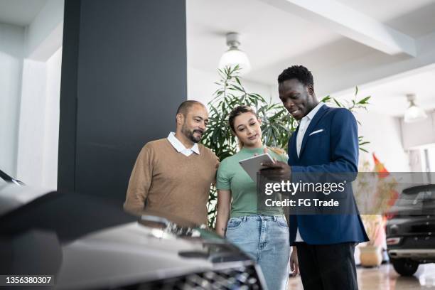 car salesman using digital tablet talking about new car to customers in a store - car salesman stockfoto's en -beelden