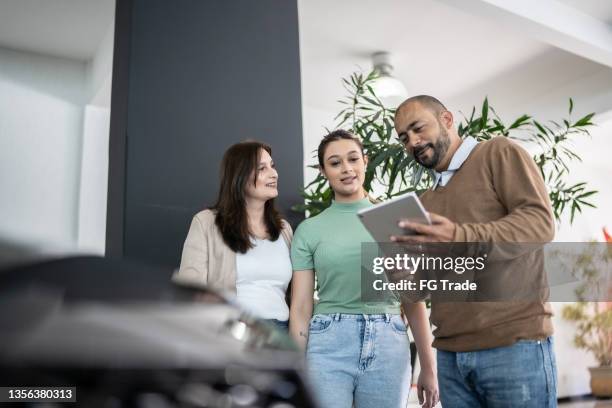 car salesman using digital tablet talking about new car to customers in a store - girl in car with ipad stock pictures, royalty-free photos & images