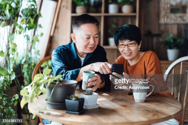 glückliches asiatisches seniorenpaar, das zu hause am tisch sitzt und gemeinsam online-banking mit mobiler app auf dem smartphone verwaltet. einfacher und sicherer zugriff auf finanzen. senioren-lifestyle. ältere menschen und technologie - asian market stock-fotos und bilder