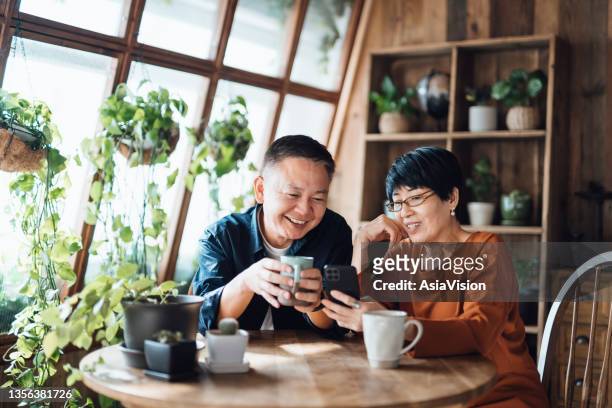 happy senior asian couple video chatting, staying in touch with their family using smartphone together at home. senior lifestyle. elderly and technology - azië stockfoto's en -beelden