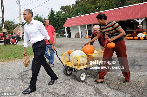 President Barack Obama pulls a cart full of pumpkin he bought at a pumpkinpatch while First Lady Michelle Obama carries two in Hampton, Virginia, on...