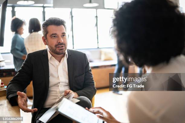 mature man talking with a colleague at work - feedback imagens e fotografias de stock