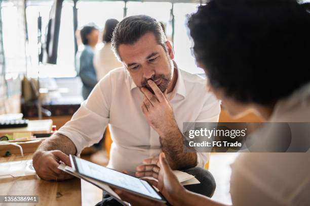 mature man looking at a digital tablet that a colleague is showing at work - problem solving stockfoto's en -beelden
