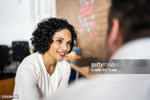 mid adult woman talking with a colleague at work - authentiek stockfoto's en -beelden