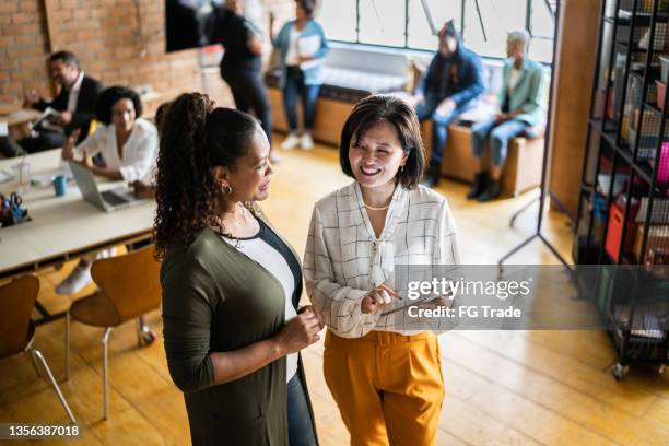 two female colleagues talking and using a digital tablet at work - oprichter stockfoto's en -beelden
