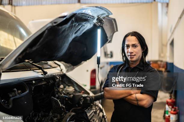 portrait of non-binary person repairing a car in auto repair shop - non binary stereotypes stock pictures, royalty-free photos & images